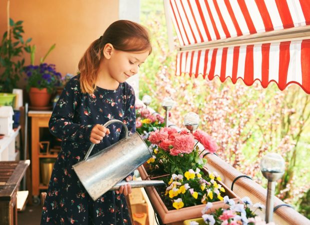 Petite fille qui arrose des plantes sur un balcon sous un Auvent rétractable motorisé rouge et blanc